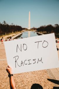 white sign with black letters saying No to Racism, held up by protester with the Washington Monument in the distance
