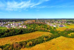 View looking out over golden fields crisscrossed with strips of forest and a small town in the distance, under a bright blue sky with wispy clouds