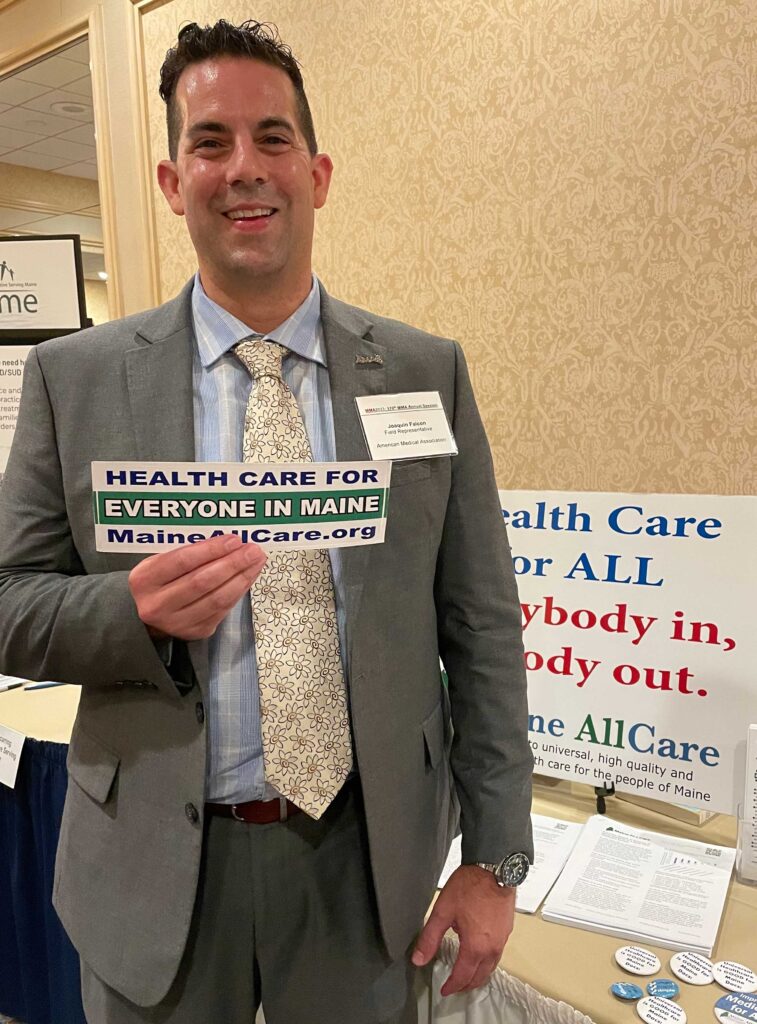 Joaquin Falcon, field representative for the American Medical Association, holds a bumper sticker saying Healthcare for Everyone in Maine, MaineAllCare.org, at the Maine Medical Association annual meeting, September 2023.
