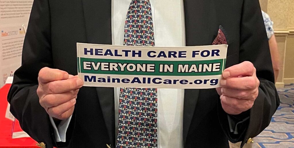 Close up of TR Reid, American filmmaker and author, holding a bumper sticker that says Healthcare for Everyone in Maine, Maine AllCare.org, at the Maine Medical Association annual meeting in September 2023.