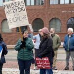 Two women holding protest signs: Mainers are Dying for Healthcare, Fund Care, Not Billionaires