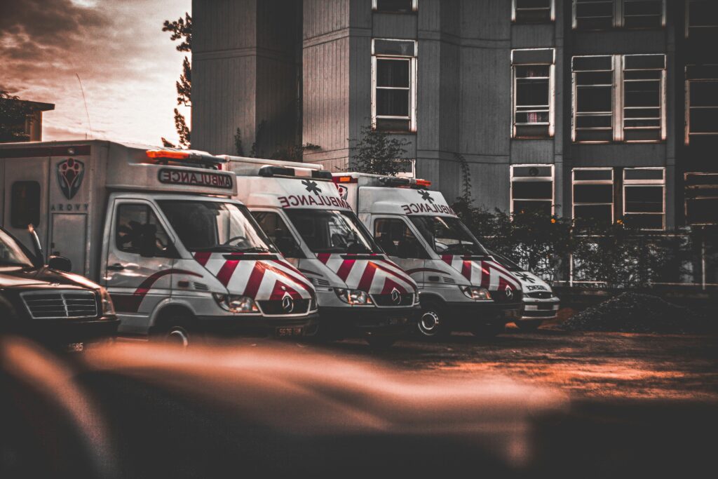 A row of ambulances outside a hospital building at sunset.