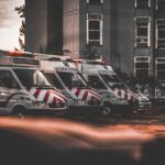 A row of ambulances outside a hospital building at sunset.